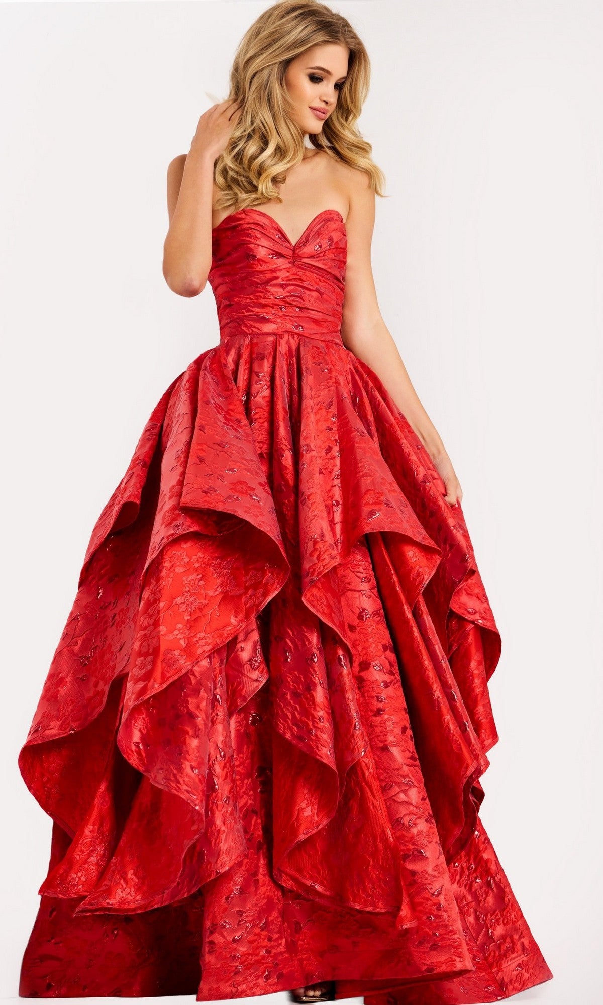 A woman wears a red strapless Jovani 47394 long prom dress featuring a textured, layered, voluminous skirt, standing against a plain background.